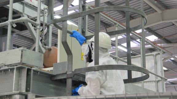 A person wearing a white safety suit climbs the ladder of the Big Rig facility