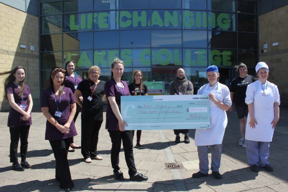 Four beauty students stand with two catering students with a large cheque