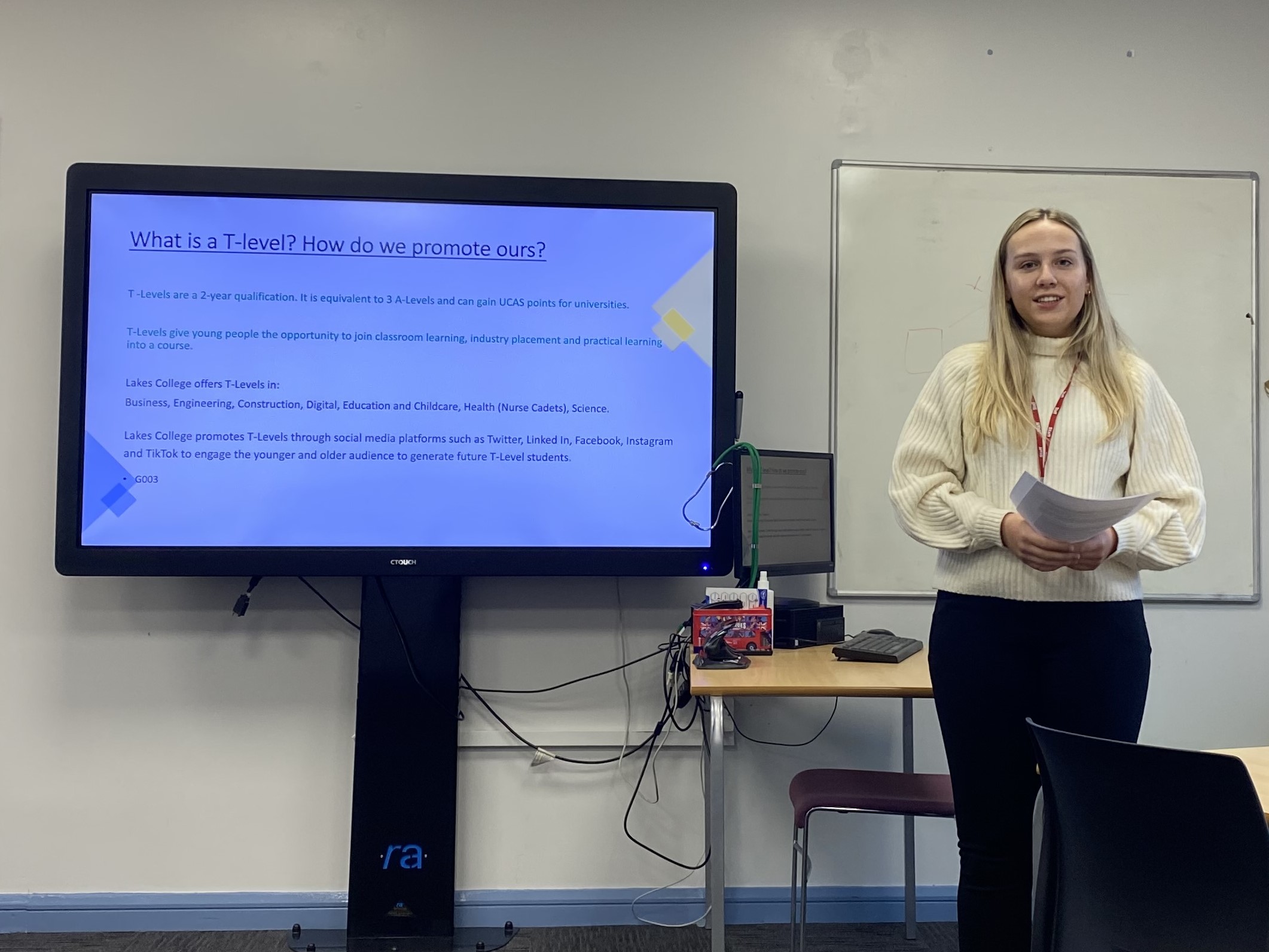 A girl with blonde hair stands in front of a computer screen to give a presentation