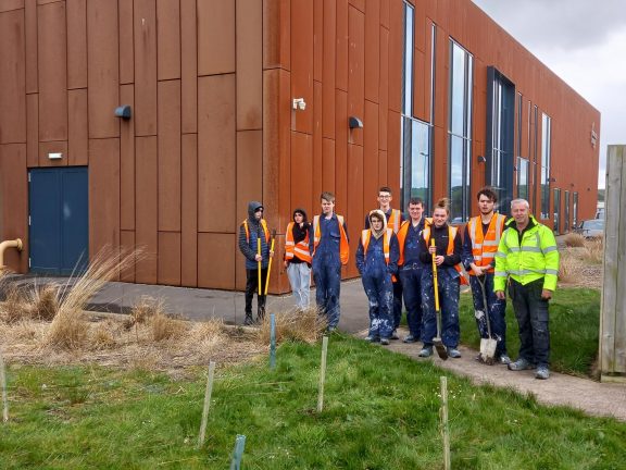 Students stand behind trees they have planted at Lakes College