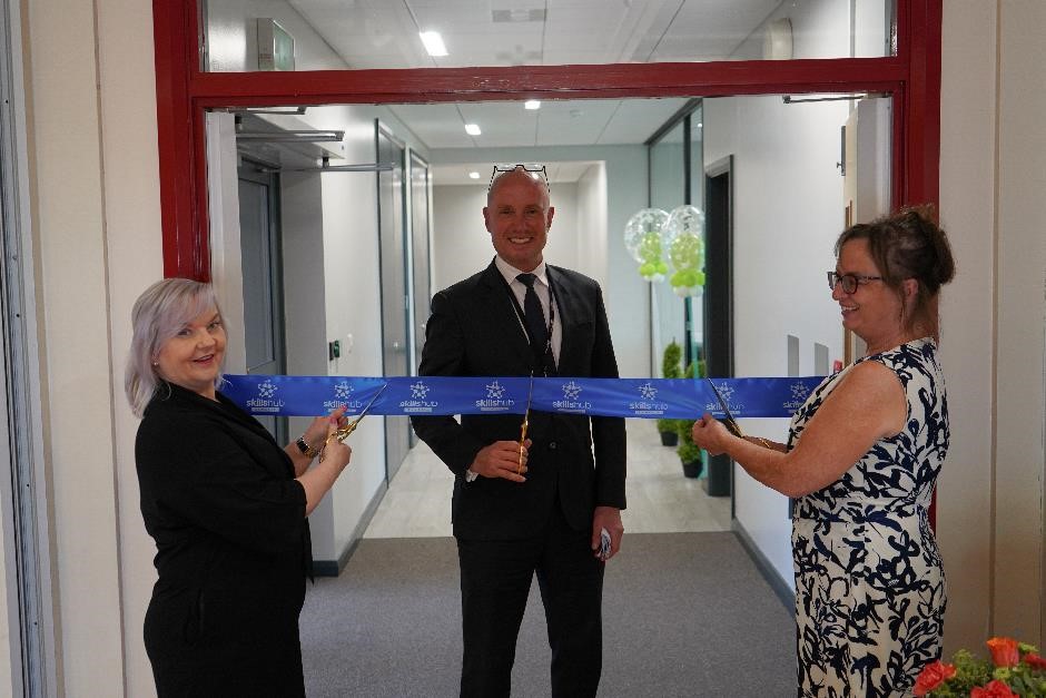 A man stands between two women as they pose before cutting a ribbon with scissors