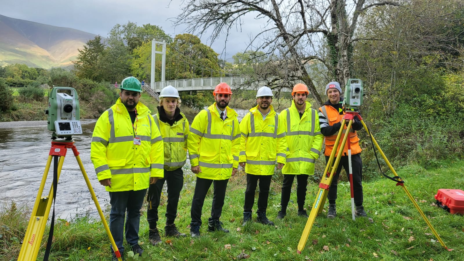 Six people stand behind total stations before carrying out a survey of a bridge