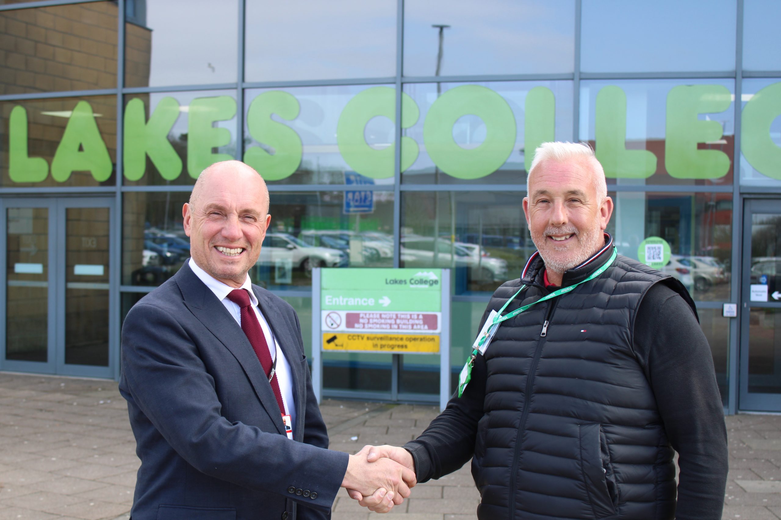 Two men shake hands in front of a building