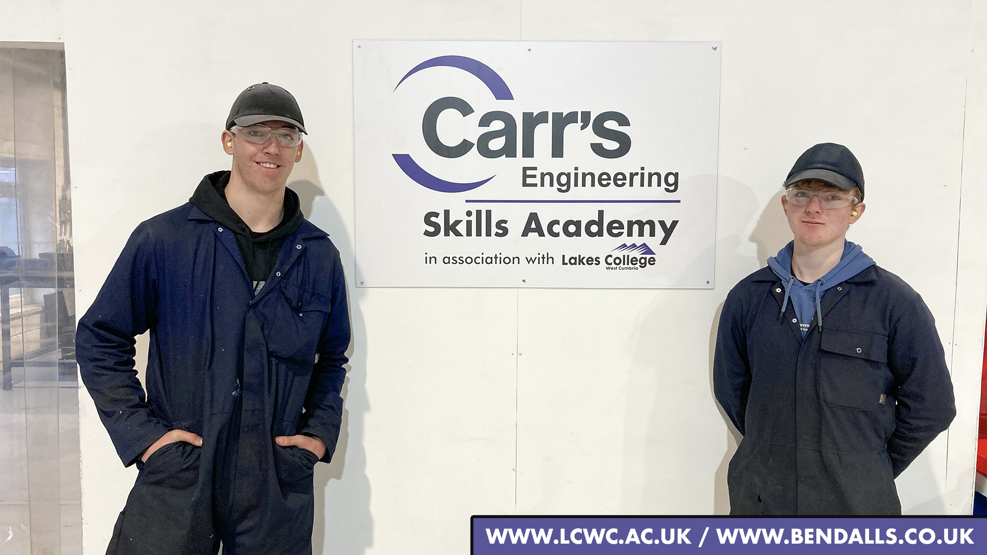 Two apprentices stand next to a sign for the Carr's Engineering Skills Academy in association with Lakes College