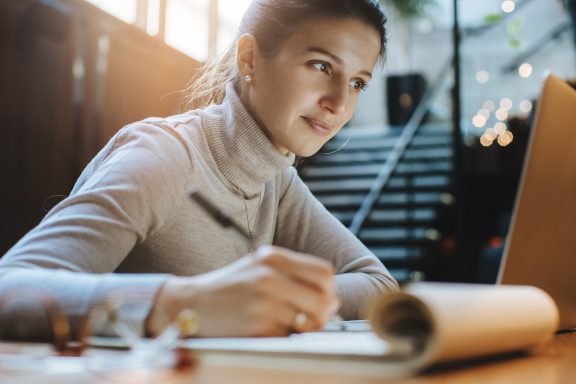 Woman making notes while working on laptop